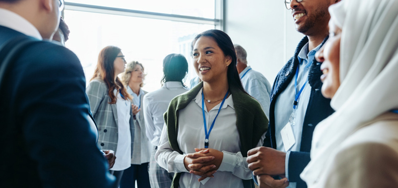 A group of people are mingling in a well-lit room. A woman in the center smiling