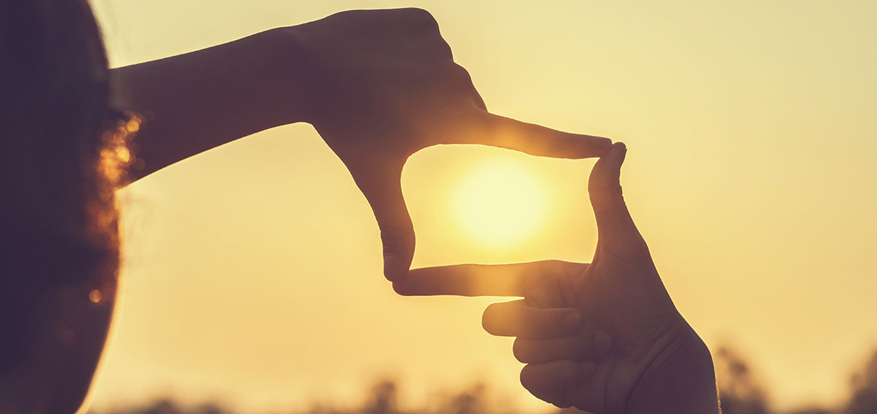 Hands framing the setting sun.