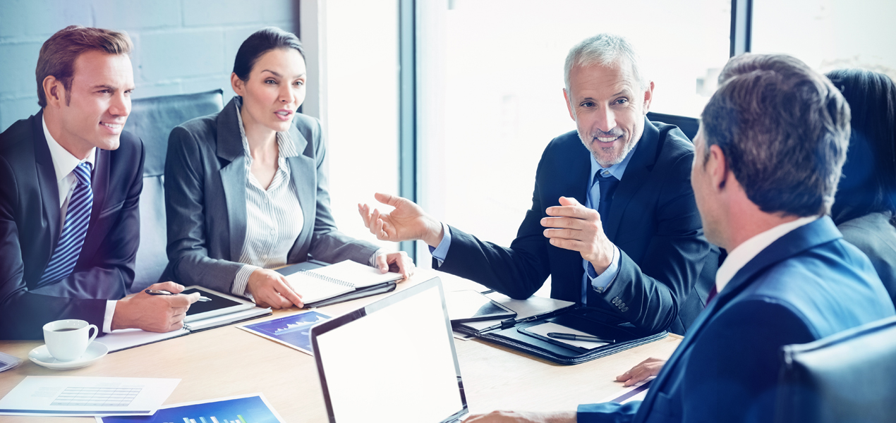 A group of business professionals engaged in a meeting around a conference table, discussing strategies and ideas.