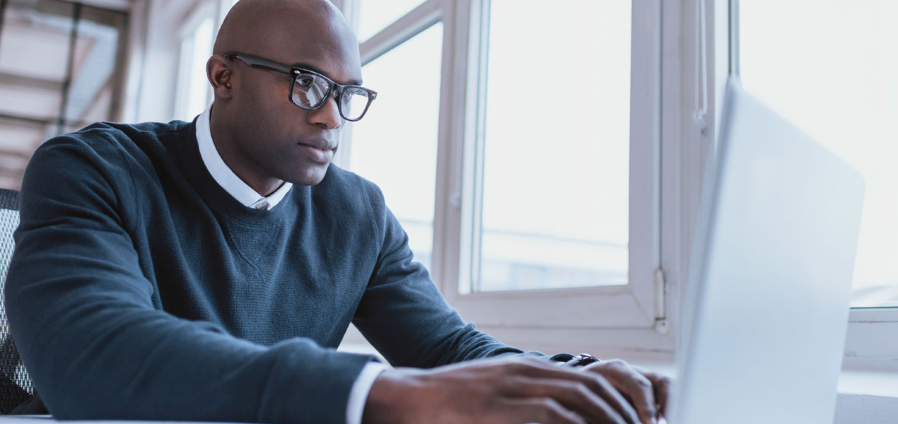 A business man working on a laptop by a large window.