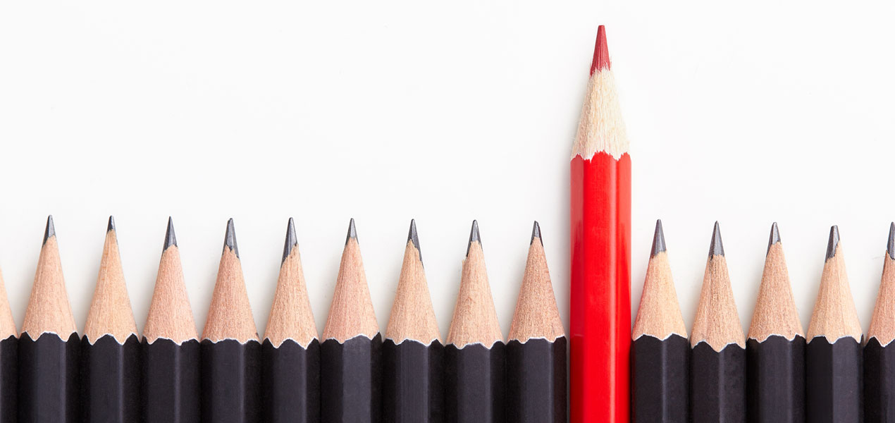 A line of black pencil crayons with one red pencil crayon standing taller.